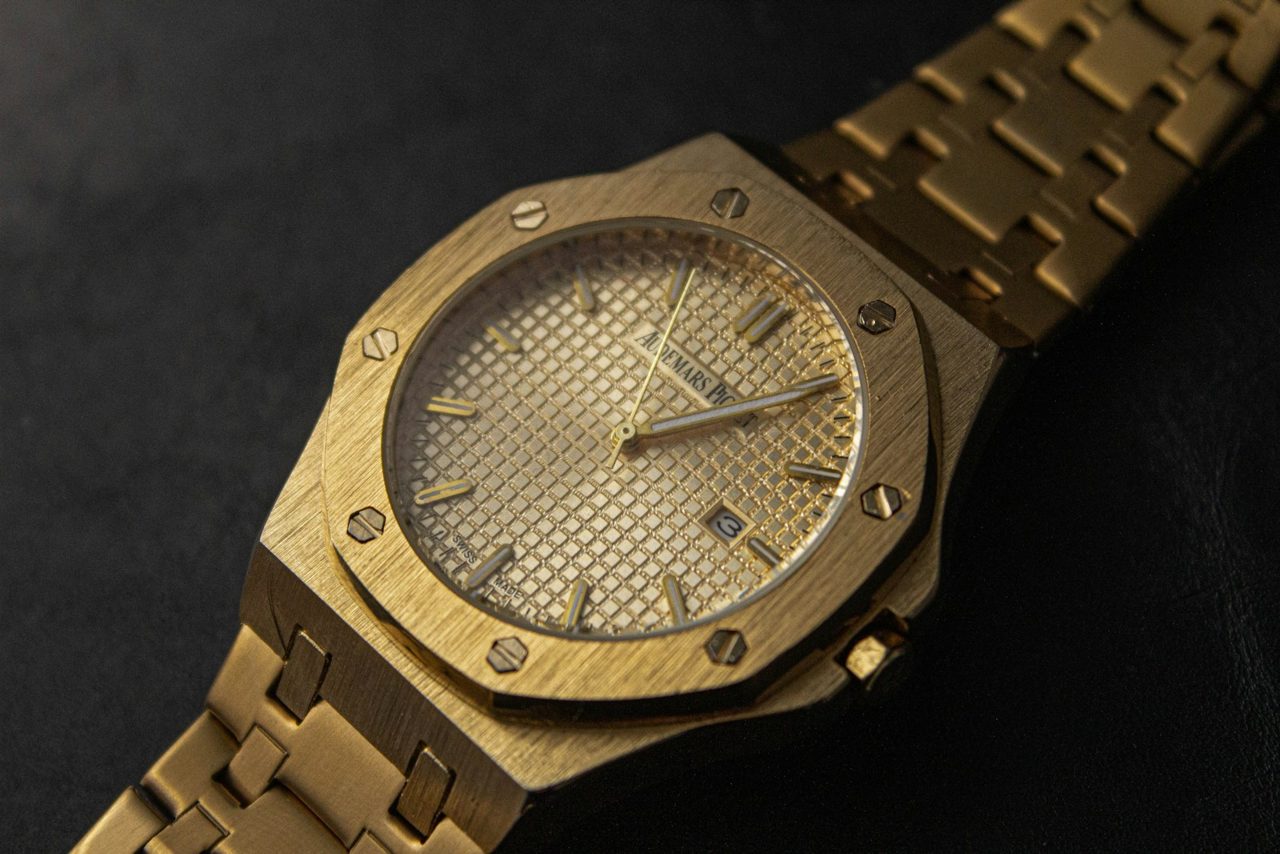 Gelbgoldene Audemars Piguet Royal Oak mit goldenem Tapisserie-Zifferblatt und integriertem Goldband auf dunklem Untergrund