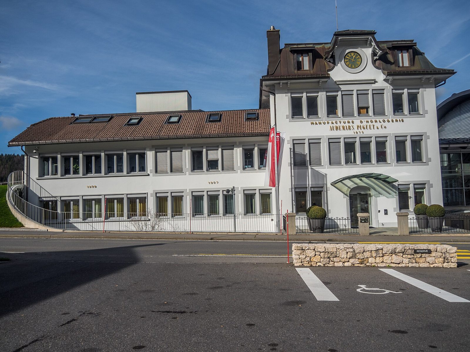Weisses Gebäude mit braunem Dach und Uhr im Giebel, an der Fassade die Aufschrift «Manufacture d'horlogerie Audemars Piguet & Co 1875»