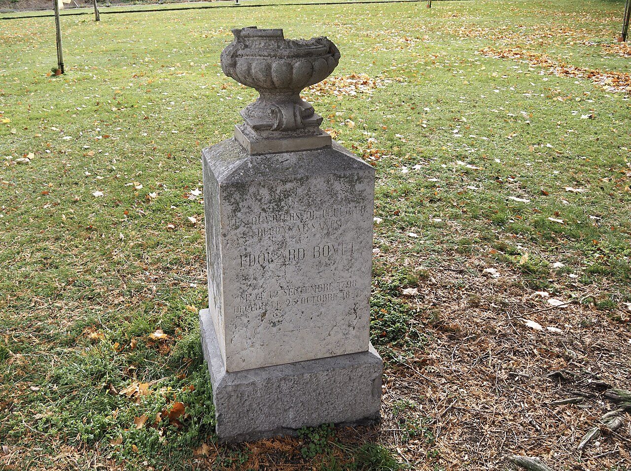 Steinernes Denkmal mit Ziervase auf einer Wiese mit Herbstlaub; die Inschrift nennt die dankbaren Arbeiter von Fleurier, Édouard Bovet sowie seine Geburts- und Todesdaten 1798 und 1849