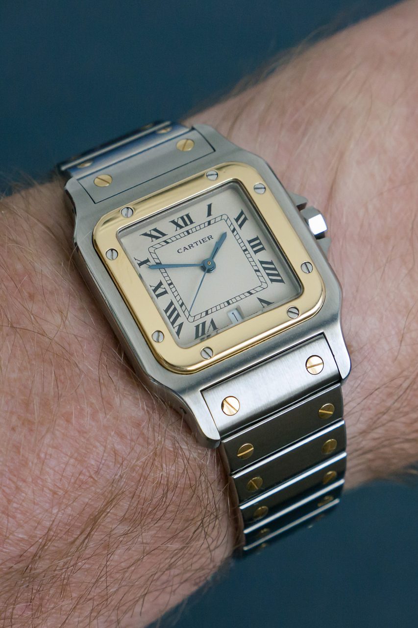 Quadratische Cartier Santos aus Stahl mit goldener Lünette und goldenen Schrauben am Gehäuse und am verschraubten Metallarmband, am Handgelenk getragen
