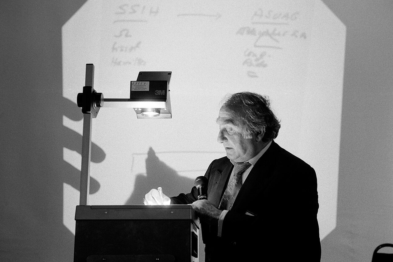 Schwarz-Weiss-Foto: Nicolas G. Hayek an einem Hellraumprojektor beim 23. Internationalen Management-Gespräch an der Universität St. Gallen