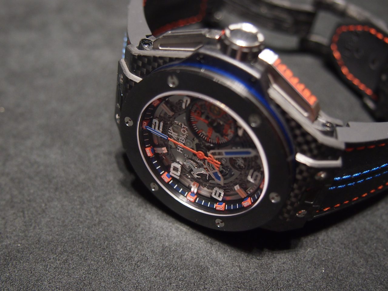 Hublot Big Bang Ferrari (Taiwan Edition) mit Gehäuse aus Carbon und Keramik, skelettiertem Zifferblatt und rot-blau abgesetztem Armband, schräg von oben auf grauem Samt fotografiert.