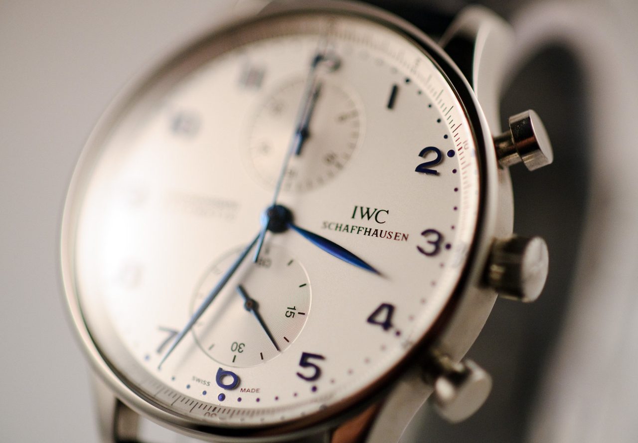 Schräge Nahaufnahme einer IWC Portugieser Chronograph mit weissem Zifferblatt, blauen Zeigern und arabischen Ziffern; die linke Bildseite ist bewusst unscharf.