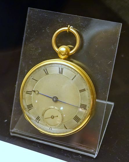 Goldene Taschenuhr mit silbrig guillochiertem Zifferblatt, römischen Ziffern, kleiner Sekunde und blauen Stahlzeigern auf einem durchsichtigen Ständer
