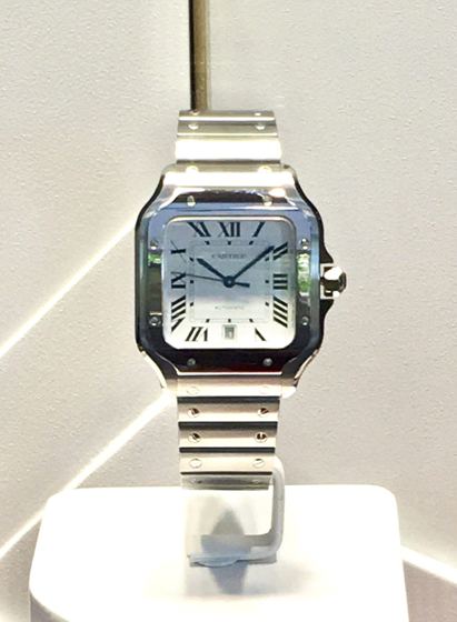 Quadratische Stahluhr mit sichtbaren Schrauben an Lünette und Armband und silbernem Zifferblatt mit römischen Ziffern auf einem Ständer
