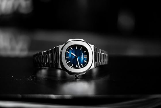 Patek Philippe Nautilus aus Stahl mit blau verlaufendem, horizontal gerilltem Zifferblatt vor schwarz-weissem Hintergrund