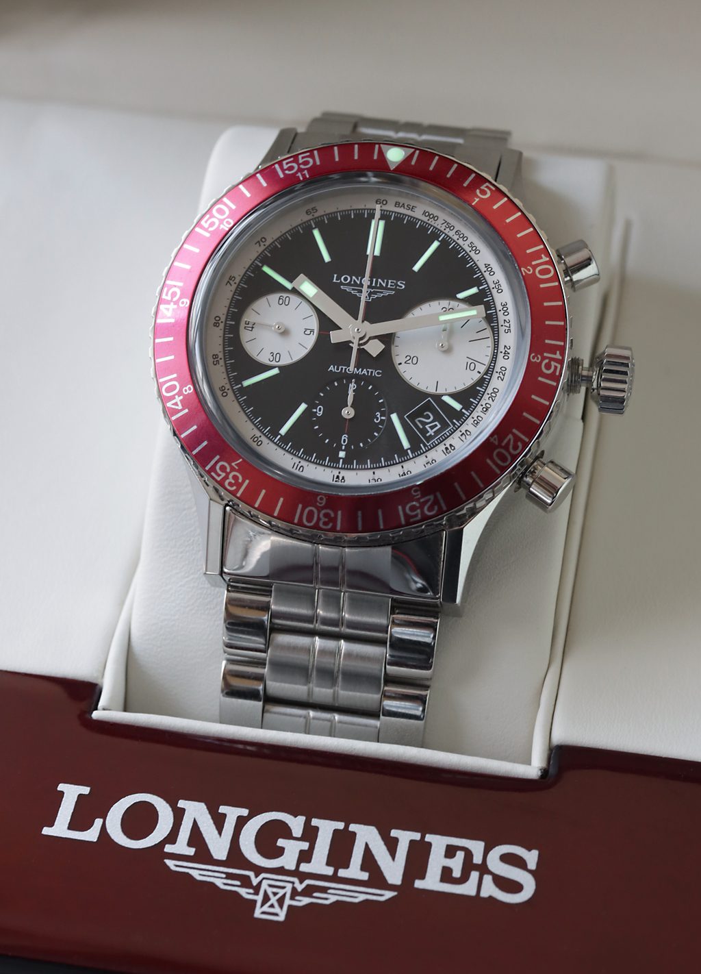 Stahl-Chronograph mit schwarzem Zifferblatt, zwei weissen Hilfszifferblättern und roter Drehlünette in einer Schmuckschachtel