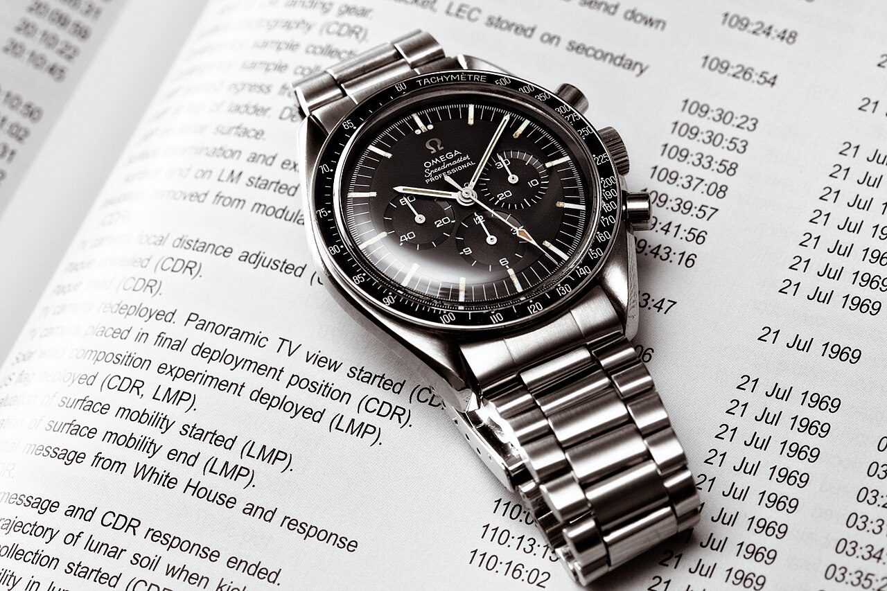 Schwarz-weiss gehaltene Omega Speedmaster Professional mit Stahlband, schräg liegend auf einer Buchseite mit Zeitangaben vom 21. Juli 1969.