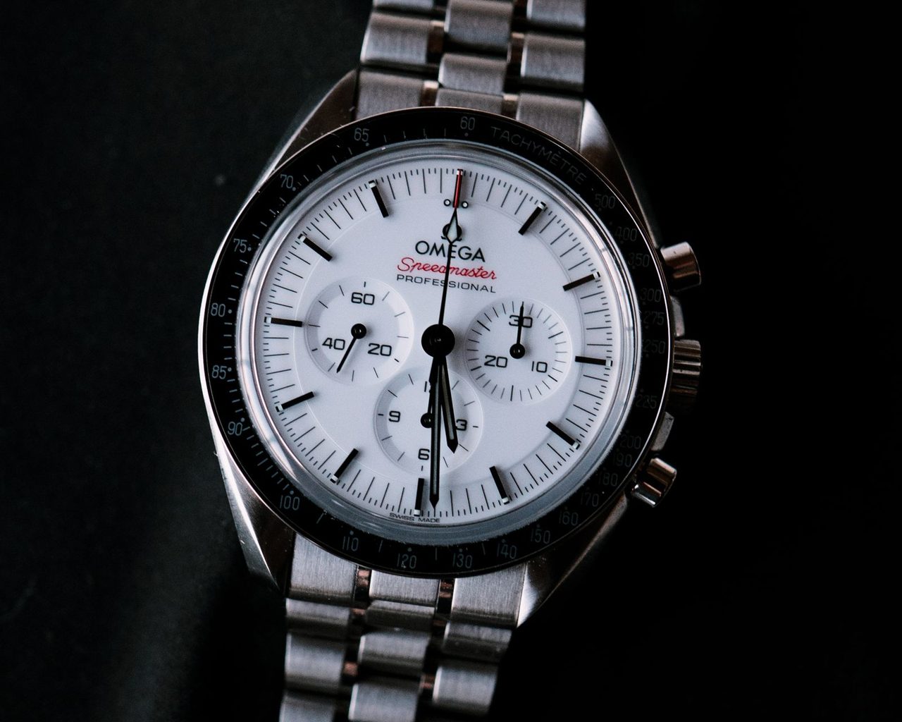 Omega Speedmaster Professional mit weissem Zifferblatt, schwarzer Tachymeterlünette und Stahlband vor schwarzem Hintergrund