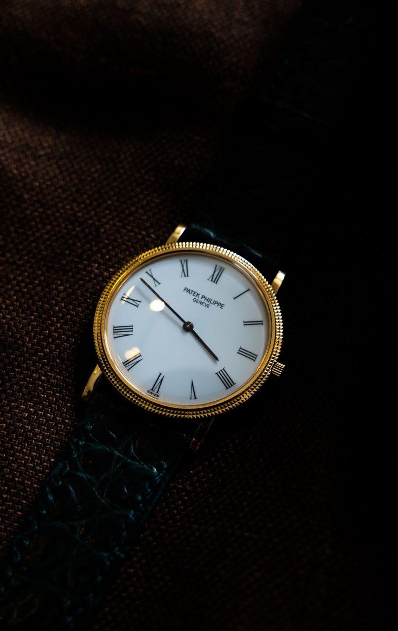 Goldene Patek Philippe Calatrava mit weissem Zifferblatt, römischen Ziffern und Clous-de-Paris-Lünette auf dunklem Stoff