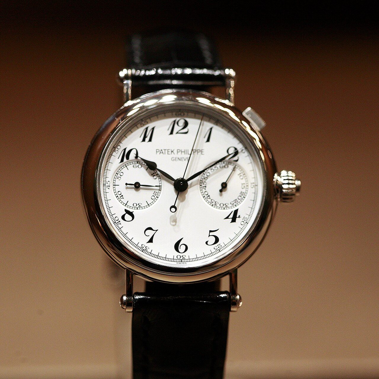 Runde Patek Philippe mit weissem Emailzifferblatt, schwarzen Breguet-Ziffern und zwei Hilfszifferblättern an schwarzem Lederband, frontal vor dunklem Hintergrund