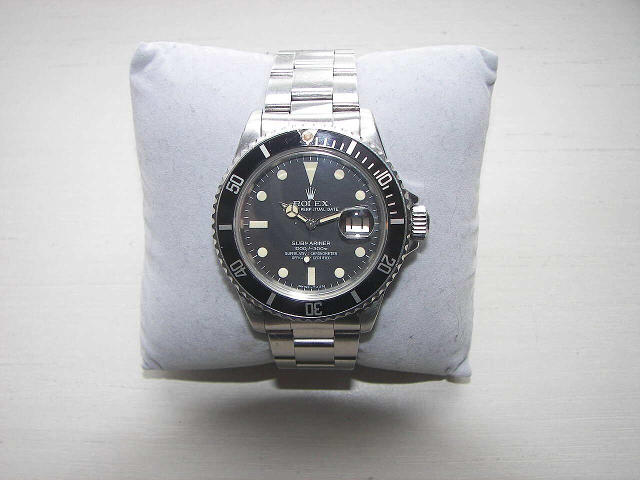 Rolex Submariner aus Stahl mit schwarzem Zifferblatt, schwarzer Drehlünette, Datumsfenster mit Lupe und Gliederband auf einem hellgrauen Kissen