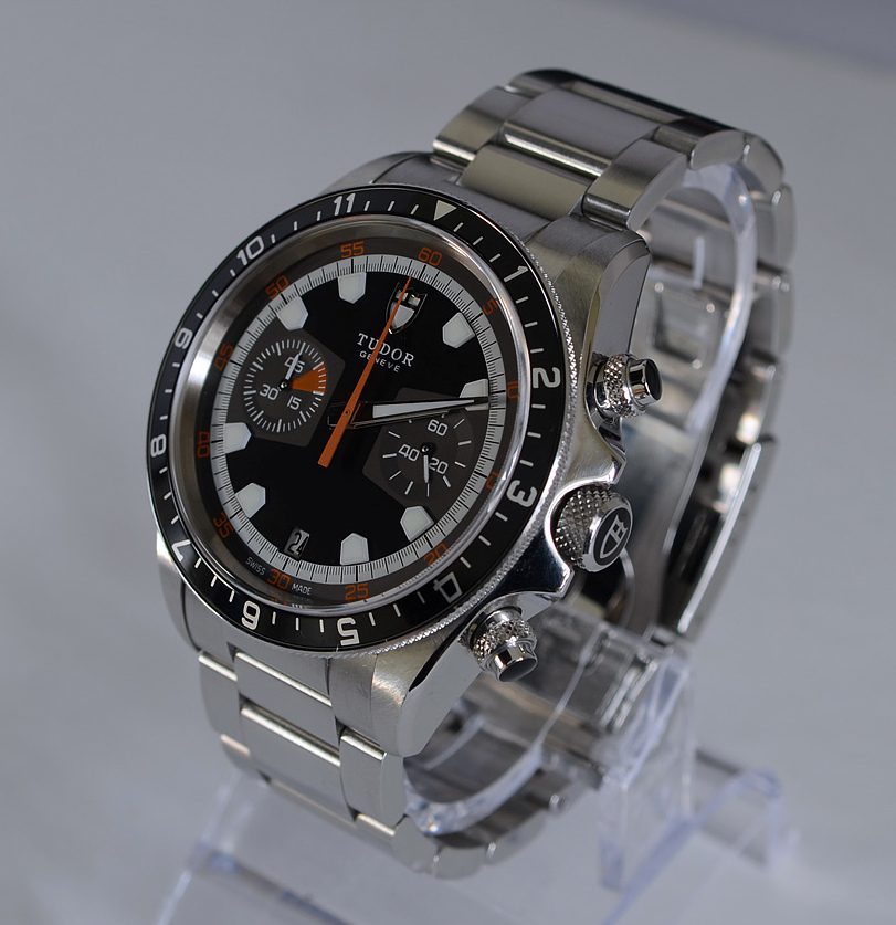 Stahl-Chronograph mit schwarzem Zifferblatt, orangem Sekundenzeiger, drei Hilfszifferblättern und schwarzer Lünette mit Zahlen an einem Stahlarmband, schräg von der Seite fotografiert