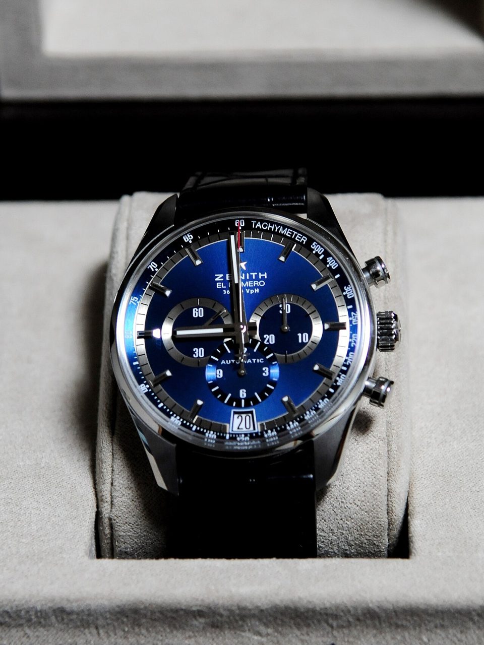 Zenith El Primero mit blauem Zifferblatt, drei Hilfszifferblättern, Tachymeterskala und Datumsfenster an einem schwarzen Lederband auf einem hellen Uhrenkissen